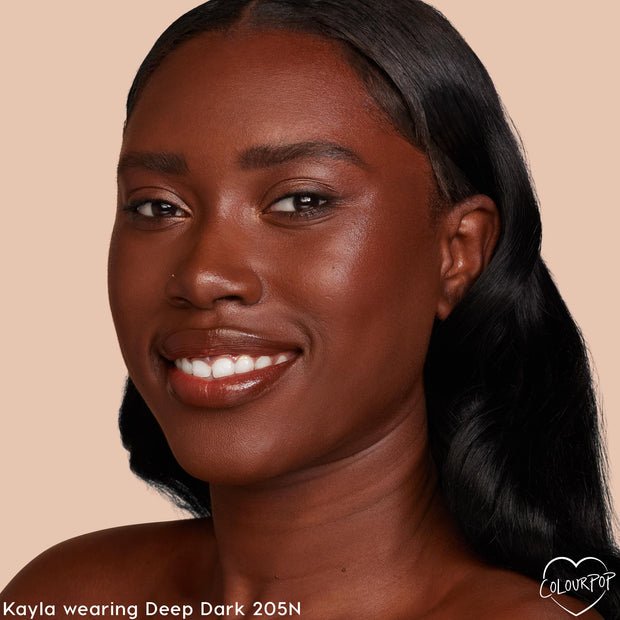 ColourPop Hyaluronic Hydrating Foundation in Deep Dark 205 N (neutral) creating a dewy, even finish on a smiling model’s face; close-up on a warm beige backdrop highlights smooth, hydrated skin and natural glow.