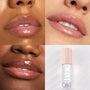 Glossy lips wear Dew Drop Lux Lip Oil, a clear high-shine ColourPop Lux Lip Oil, across three close-up swatches on different skin tones, with the LUX lip oil bottle and star-print blush pink cap shown on a white wavy backdrop.