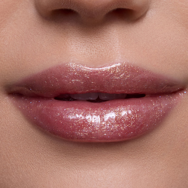 Close-up of slightly parted lips wearing Ambitious Tiana Ultra Glossy Lip, a shimmering pink-nude Disney Princess lip gloss with high-shine, glittery finish on smooth, natural skin in studio lighting.