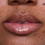 Close-up of glossy, medium-toned lips wearing Ambitious Tiana Ultra Glossy Lip, showing shimmering gold and pink sparkle inspired by Disney Princess beauty, with natural skin and freckles softly visible around the mouth.