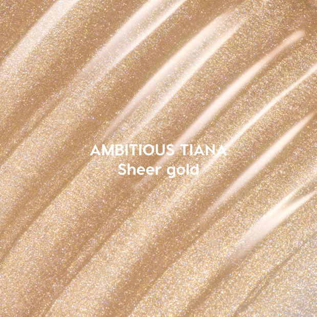 Ambitious Tiana Ultra Glossy Lip swatched in diagonal streaks of shimmering sheer gold, showcasing a sparkling Disney Princess–inspired lip gloss shade on a close-up textured background.