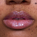Close-up of freckled lips wearing Courageous Rapunzel Ultra Glossy Lip, a shimmering pink-lilac Disney Princess lip gloss with high-shine, iridescent sparkle on medium skin tone, showing smooth, hydrated finish and vivid color payoff.