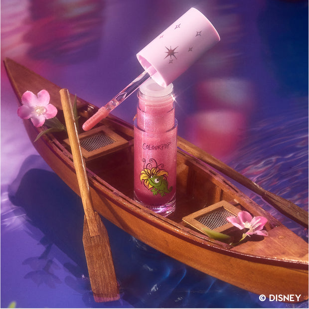 Courageous Rapunzel Ultra Glossy Lip from the Disney Princess collection stands open in a wooden boat, its pink glitter lip gloss wand hovering above the tube against a purple water background with floating flowers, styled for US beauty lovers.