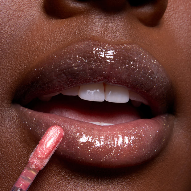 Close-up of glossy, sparkly lips as a wand applies Mademoiselle Belle Ultra Glossy Lip, a shimmering nude Disney Princess lip gloss, highlighting high-shine finish and fine glitter detail for a glamorous makeup look.