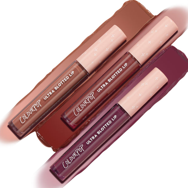 Three ColourPop Ultra Blotted Lip tubes from the Edgy Vibes set lie diagonally over swatches, displaying warm nude, brick red, and berry plum shades with pink star caps, highlighting a soft-matte, blurred lip finish.