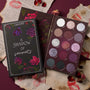 ColourPop A Shadow of Secrets shadow palette displays 15 shades - mauve, plum, silver, and charcoal - mix of mattes and sparkles, opened beside its floral box on a burgundy backdrop with torn pages, lipstick kisses, and dried roses; a romantic ColourPop Shadow Palette.