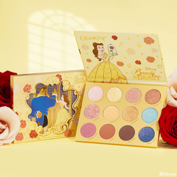 ColourPop Shadow Palette Beauty and the Beast opens to show 12 pans in pinks, golds, corals, and blues with matte and glitter finishes, Belle art on a yellow case, with matching box and roses on a soft yellow background.