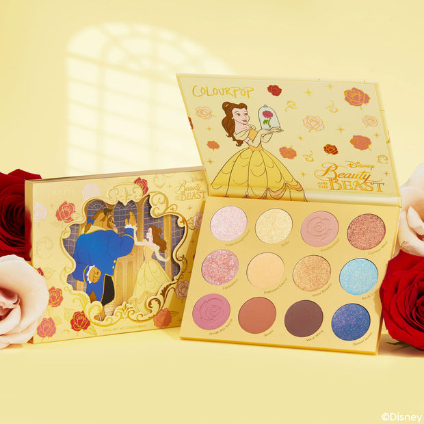 ColourPop Shadow Palette Beauty and the Beast opens to show 12 pans in pinks, golds, corals, and blues with matte and glitter finishes, Belle art on a yellow case, with matching box and roses on a soft yellow background.