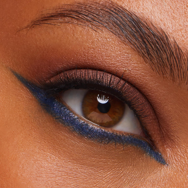 Brown eye wearing warm copper matte shadow and a precise cobalt-blue winged liner, highlighting blended pigment and natural lashes; studio close-up showcasing the As Old As Time Shadow Palette, Cheek & Lip Set from ColourPop.