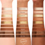 Feelin' Toasty ColourPop Shadow Palette swatches displayed on three arms, labeled Baked Goods, Slow Burn, Cinder Up, Marshmallow Me, Firestarter, Spiced Rum, Smolder, Cinna-Bun, and Cozy Vibez, warm mattes and metallic golds across varied skin tones.