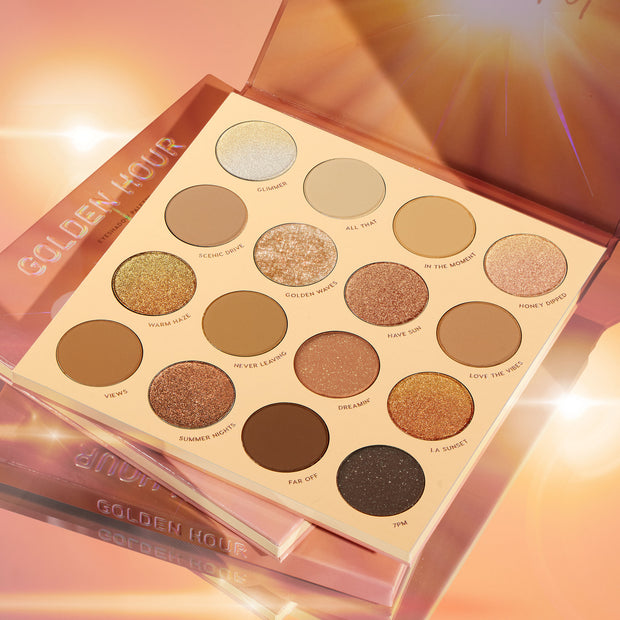 Golden Hour ColourPop Shadow Palette opened to 16 warm-tone pans - mattes and metallic gold, bronze, and copper shimmers like Glimmer, Golden Waves, and LA Sunset - sparkling under sun flares on a glossy peach background with stacked packaging.