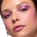 Violet and lilac shimmer blended across lids on a model, showcasing the ColourPop It’s My Pleasure shadow palette; close-up beauty shot with soft pink blush, defined lashes, and glossy pink lips on dewy skin.