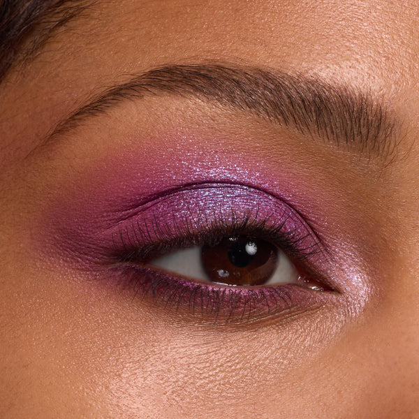 Shimmery violet‑magenta eyeshadow blends across the lid, crease, and lower lash line with a metallic inner‑corner highlight, showcasing the It’s My Pleasure ColourPop Shadow Palette in a tight macro of the eye and groomed brow.