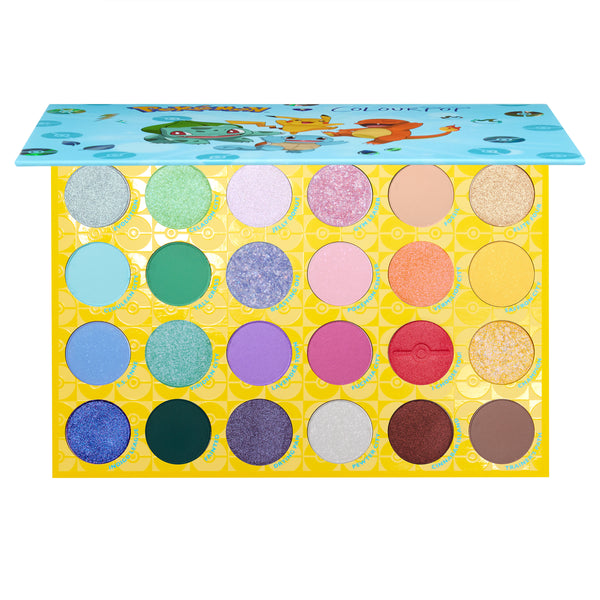 Open ColourPop Shadow Palette Pallet Town shows 24 eyeshadows - mattes and shimmers in blues, greens, purples, pinks, golds, and neutrals - set in a yellow Poké Ball tray with a blue Pokémon lid featuring Pikachu, Charmander, and Bulbasaur.