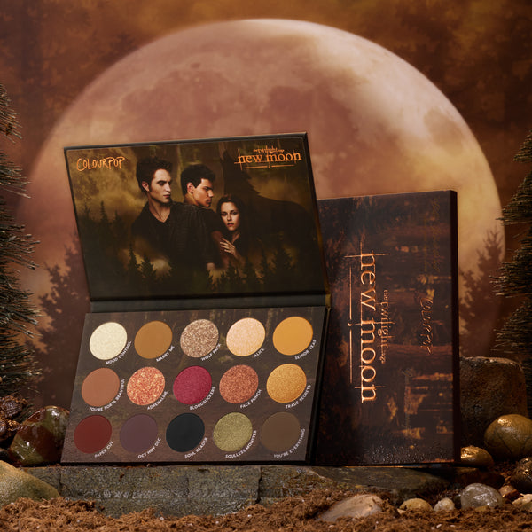 New Moon ColourPop Shadow Palette opens to 15 warm neutrals and vampy tones in matte and shimmer - gold, copper, berry, and olive - with Twilight: New Moon artwork of three characters under the lid, styled on forest rocks against a large moon backdrop.