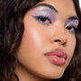 Model shows icy lavender and periwinkle winged eyeshadow with blue lower‑lash liner and silver shimmer, showcasing the Beach Dreamin' ColourPop Shadow Palette; dewy glow, pink blush, and glossy nude lips in a close‑up studio beauty shot.