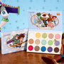 ColourPop The Toys Are Here shadow palette displaying a mix of bright and neutral matte and shimmer shades, packaged with Toy Story art of Woody, Buzz Lightyear, Jessie, Rex, and friends on a wood table against a sky-blue sheriff-badge backdrop.