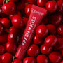 ColourPop Fresh Kiss Glossy Lip Balm in Cherry Glaze rests among glossy red cherries in a top-down flatlay, showcasing the Fruit Basket Glossy Lip Balm Trio - ColourPop Glossy Lip Balm Trio offering hydrating, high-shine cherry tint.