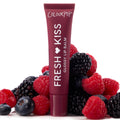 ColourPop Fresh Kiss Glossy Balm in Wild Berry standing upright, deep berry tube with white lettering nestled among fresh raspberries, blackberries, and blueberries on a white backdrop, highlighting juicy, glossy lip care.