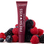 ColourPop Fresh Kiss Glossy Balm in Wild Berry standing upright, deep berry tube with white lettering nestled among fresh raspberries, blackberries, and blueberries on a white backdrop, highlighting juicy, glossy lip care.