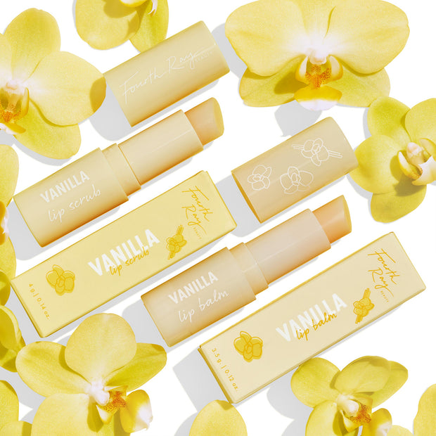 Vanilla Kisses Lip Care Set showcases ColourPop Lip Scrub and lip balm, tubes uncapped to reveal product, in soft-yellow Fourth Ray Beauty packaging with orchid graphics, arranged flat on a white background among yellow orchid flowers.