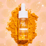 Turmeric Serum face serum bottle with a white dropper cap stands on a mound of turmeric powder, filled with golden liquid and surrounded by glossy serum drops on a peach background; Fourth Ray Beauty 0.50 fl oz ColourPop Face Serum.