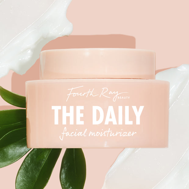 Peach-pink jar of The Daily Face Cream by Fourth Ray Beauty resting on glossy green leaves, flanked by white cream swipes on a blush background, highlighting this hydrating ColourPop Face Moisturizer for everyday use.