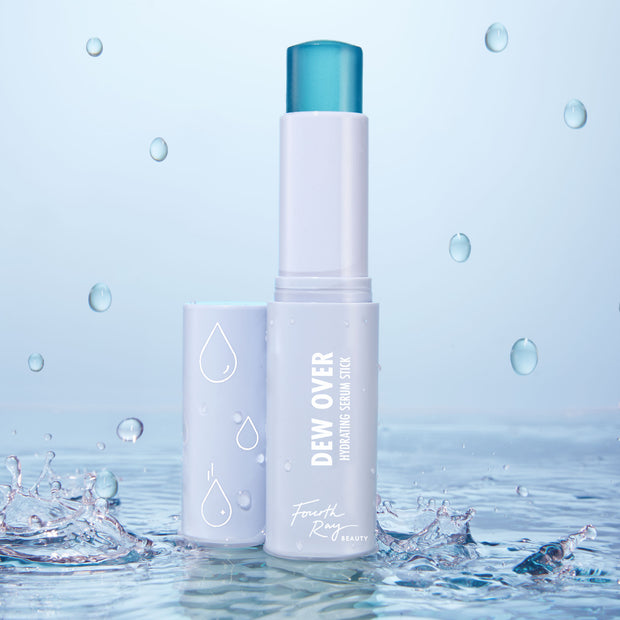 Fourth Ray Beauty Dew Over hydrating serum stick stands open showing teal balm, part of the Dew You ColourPop Face Set, with droplets and water splashes around a pastel lavender tube with raindrop icons on a light blue backdrop.