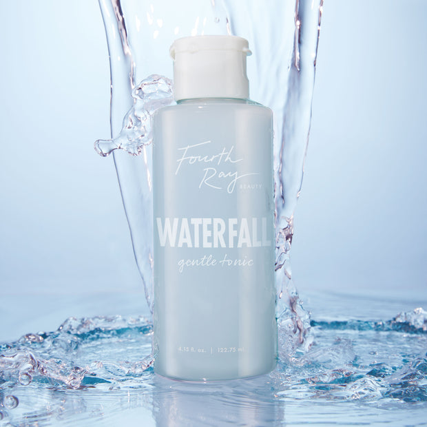 Fourth Ray Beauty Waterfall Gentle Tonic face toner standing upright as water splashes around it, showcasing a pale blue 4.15 fl oz bottle with white flip cap; hydrating ColourPop Face Toner in a fresh waterfall setting.