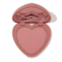 Heart-shaped dusty-rose compact opens halfway to reveal Flirt Alert, a soft rosy pink ColourPop Pressed Powder Blush in a heart pan with built-in mirror, shown on a clean white background.