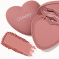 Heart-shaped compact displays ColourPop Pressed Powder Blush in Flirt Alert, a dusty rose pink, with the lid logo visible, an open mirror, and a crushed swatch smeared beside the case on a white background.