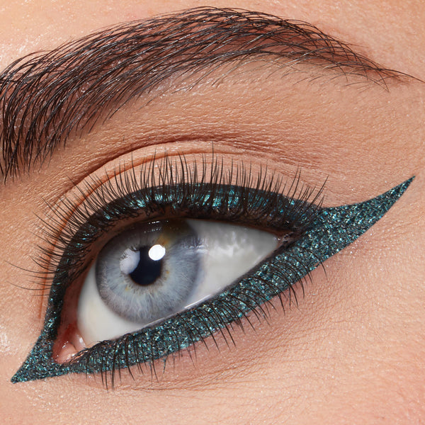 ColourPop Graphix Ink Liner in Forever defining a blue eye with a bold, elongated cat-eye; metallic teal shimmer lines upper and lower lash lines in a razor-sharp wing, framed by natural lashes and a groomed brow in a close-up.