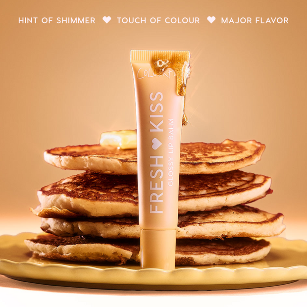 Colourpop Fresh Kiss Glossy Balm in Buttery Pancakes flavor standing upright against a stack of syrup-drizzled pancakes on a yellow plate, styled on a rich burgundy background to showcase this Lip Gloss & Lip Oil hybrid.
