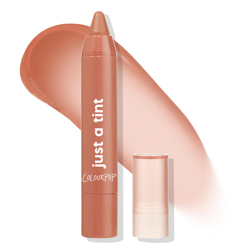 Colourpop Gimme S'more Just a Tint lip crayon stands uncapped beside its clear lid, showing a warm nude Lipstick & Lip Stains shade swatched in a smooth, glossy streak on a white background.