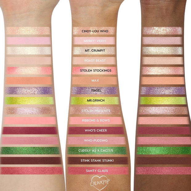ColourPop How the Grinch Stole Christmas shadow palette swatched on three forearms, showing 18 labeled shades - neutrals, pinks, cranberry, purple, metallic golds, lime green, and deep brown - demonstrating payoff across light to deep skin tones.
