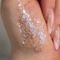 Disco Lady ColourPop Glitter Gel swatched on the back of a hand, shimmering with multicolor iridescent hex and micro-glitter in a clear gel base, catching light beside glossy nude-pink nails in a tight beauty close-up.