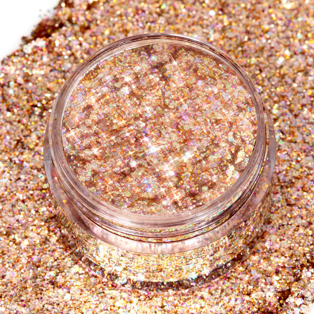 ColourPop Avenue of the Stars Glitter Gel jar sparkling as iridescent rose‑gold hex glitter catches the light, shown open in a clear pot resting on a dense swatch of matching shimmer for a close-up product texture view.