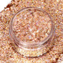 ColourPop Avenue of the Stars Glitter Gel jar sparkling as iridescent rose‑gold hex glitter catches the light, shown open in a clear pot resting on a dense swatch of matching shimmer for a close-up product texture view.