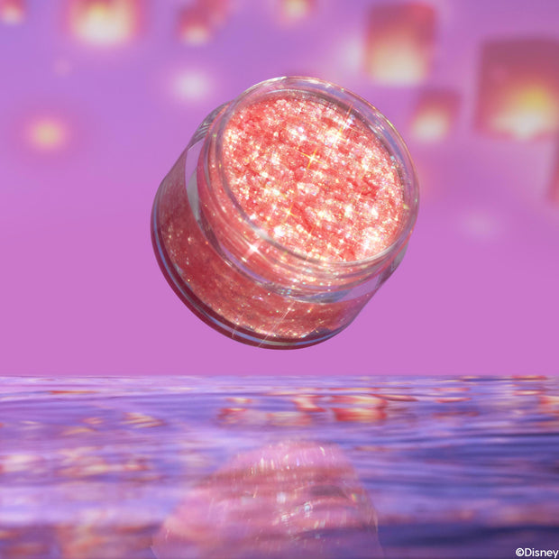 Floating Lights glitter gel jar hovers tilted above rippled water, its rosy-pink, chunky iridescent sparkles shining against a purple background with lantern bokeh; ColourPop Glitter Gel for face and body shown open, no lid.
