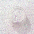 ColourPop Who-Hash glitter gel shimmers in an open clear jar, chunky iridescent white and lavender flecks catching light, set against a full background swatch of matching holographic sparkle for a close-up beauty product shot.