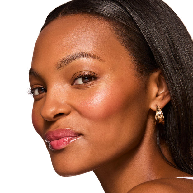 Model's lips wearing Get Rich from the ColourPop Glossy Lip Balm Trio, showing a sheer cherry-pink shine with a smooth, hydrating finish; close-up studio profile with dewy skin and a gold hoop earring.