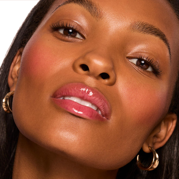 ColourPop Fresh Kiss Glossy Balm in Cherry Glaze coats lips with a juicy cherry-pink shine and cushiony, hydrated finish, showcased in a tight beauty close-up of a model wearing gold hoop earrings under soft studio lighting.