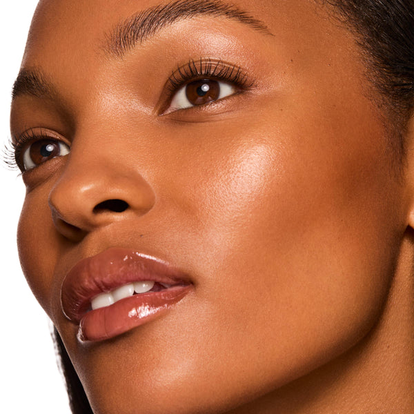 Glossy lips wearing ColourPop Fresh Kiss Glossy Balm, shade Chocolate Milkshake, catching light with a sheer chocolate-brown tint and glass-like shine in a tight studio close-up of the mouth and lower face, emphasizing smooth, hydrated lips.