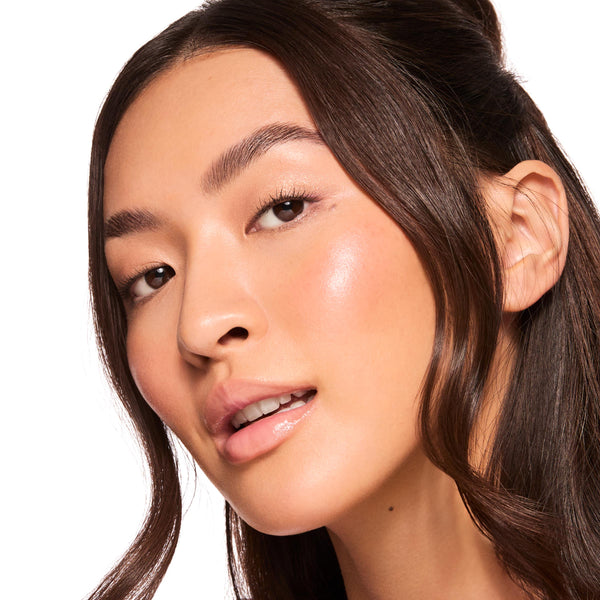 Glossy lips wearing ColourPop Fresh Kiss Glossy Balm, Mango Sorbet, catching light with a sheer peachy shine as a model tilts her face in a studio close-up, smooth hydrated finish showcasing the Fresh Kiss glossy balm texture against a white background.