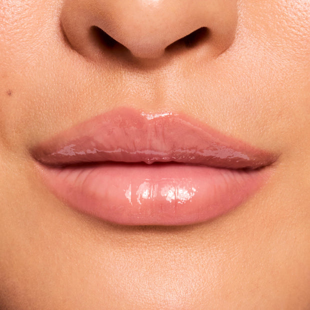 Glossy lips wearing ColourPop Fresh Kiss Glossy Balm in Strawberry Milk, reflecting a high-shine, sheer milky pink finish in a close-up swatch for a smooth, hydrated look.