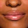Glossy lips wearing ColourPop Fresh Kiss Glossy Balm in Vanilla Cake, showing a sheer nude-pink shine and smooth, hydrated finish in a close-up lip swatch on a model under studio lighting.