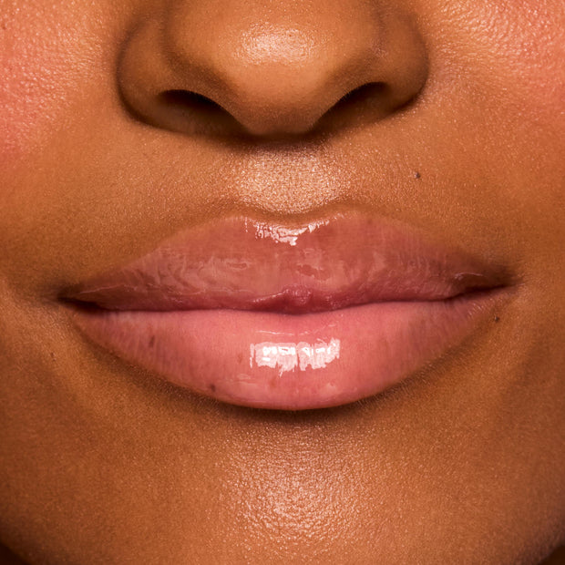 Glossy lips wearing ColourPop Fresh Kiss Glossy Balm in Vanilla Cake, showing a sheer nude-pink shine and smooth, hydrated finish in a close-up lip swatch on a model under studio lighting.