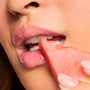 Glossy pink lips wearing Watermelon Sugar, the ColourPop Fresh Kiss Glossy Balm, softly bite a juicy watermelon slice held by manicured fingers, in a close-up studio beauty shot that showcases high-shine, hydrating color.