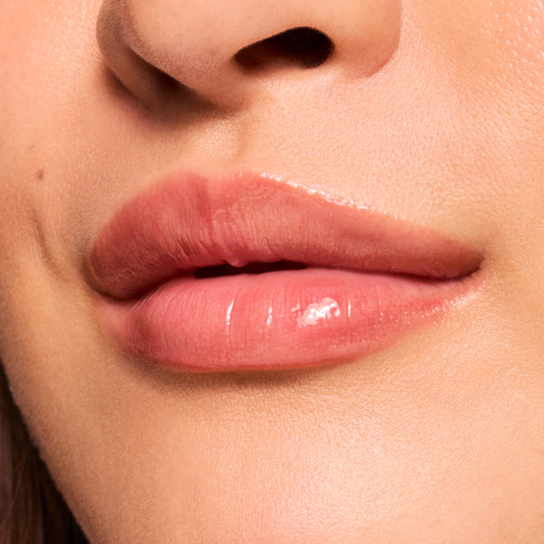Glossy lips wearing ColourPop Fresh Kiss Glossy Balm in Wild Berry, showing a sheer berry-pink tint and glassy shine in a tight macro close-up of the mouth and surrounding skin.