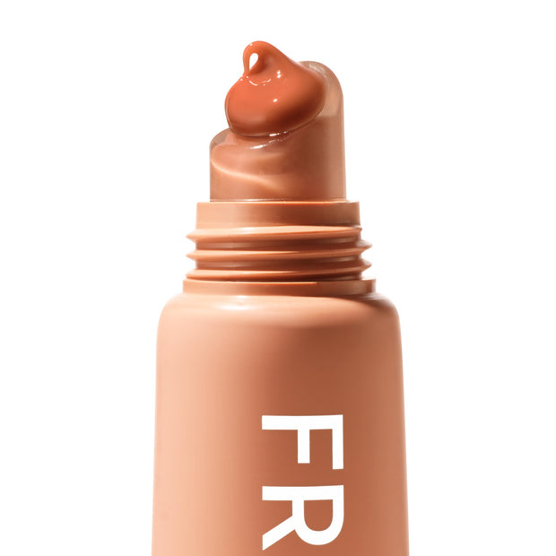 ColourPop Fresh Kiss Glossy Balm in Caramel Latte dispensing a caramel-brown dollop from a slanted rounded applicator tip, shown close-up on a peachy-nude tube with white “FR” lettering against a clean white background.